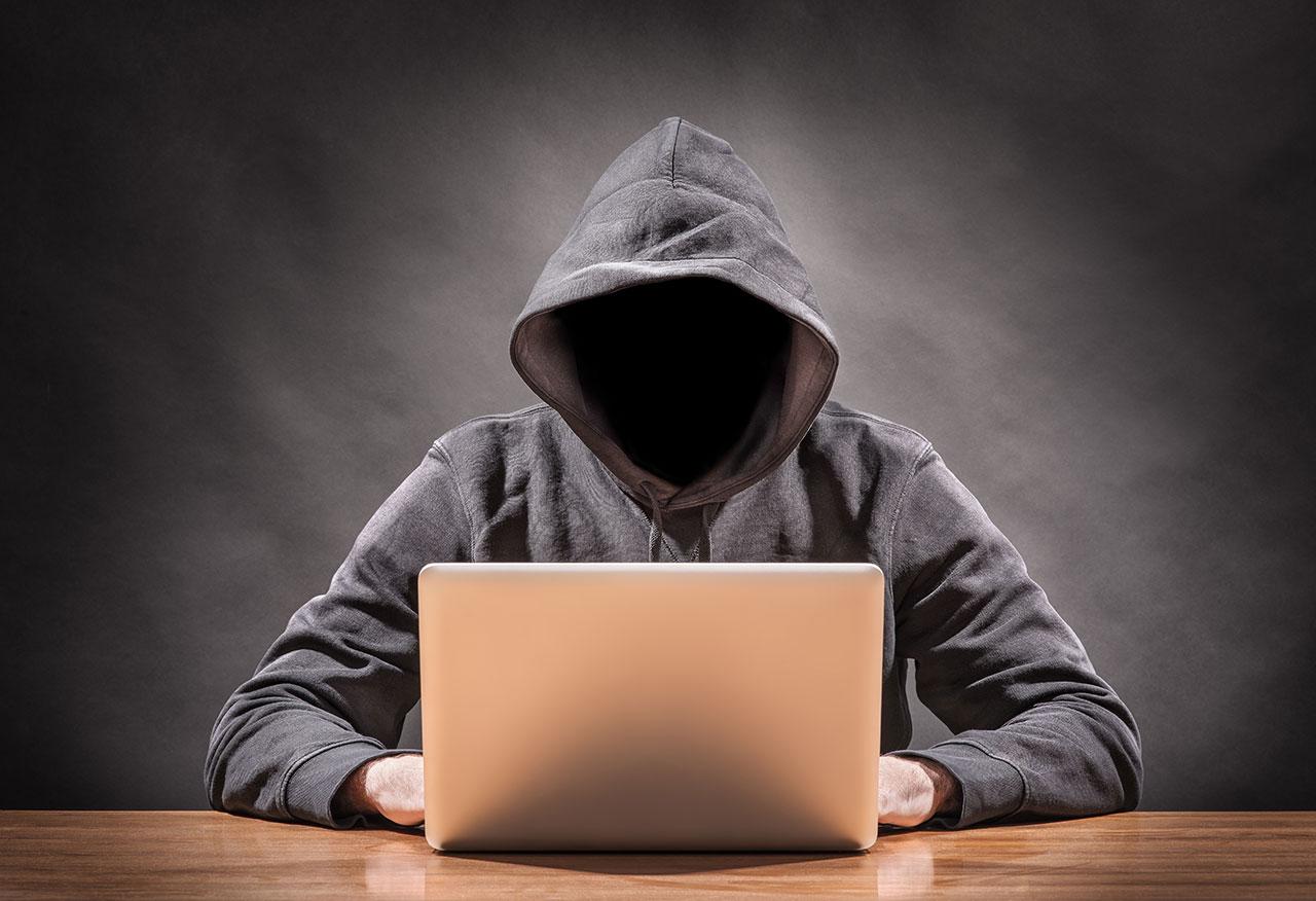 An unidentified man in a hoodie with a laptop